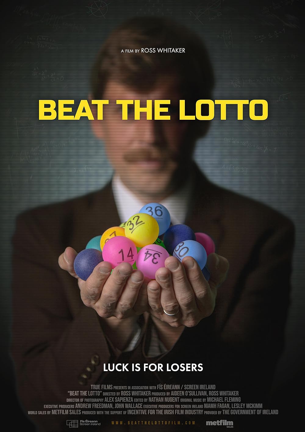 Text on poster: “Beat the Lotto.” “Luck is for Losers.” The image shows a man holding numbered lottery balls toward the viewer.