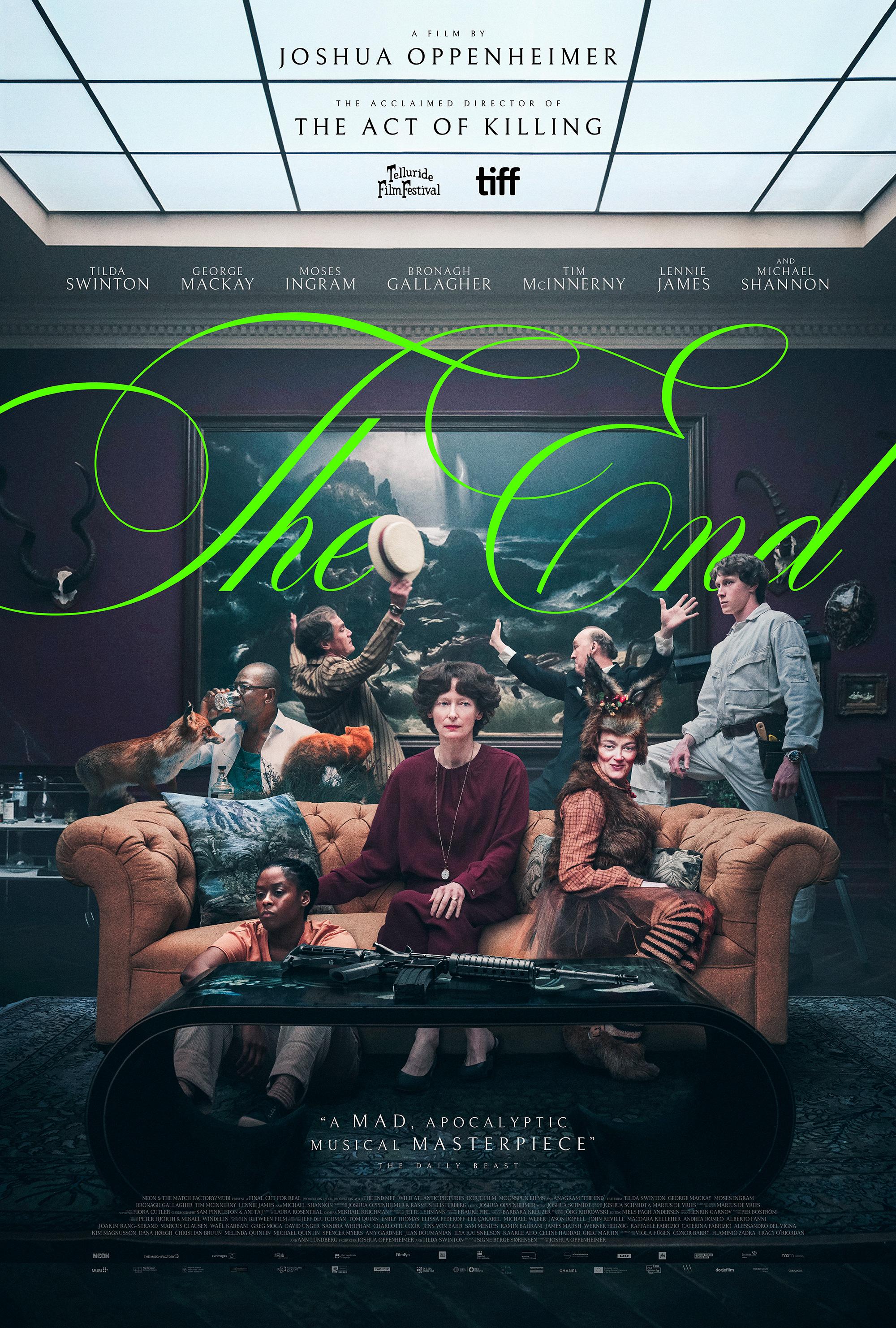 Text on poster: “The End.” A film by Joshua Oppenheimer. The image shows a staged living-room scene with multiple posed figures.