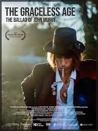 Text on poster: “The Graceless Age: The Ballad of John Murray.” The image shows a man outdoors wearing a hat, looking downward.