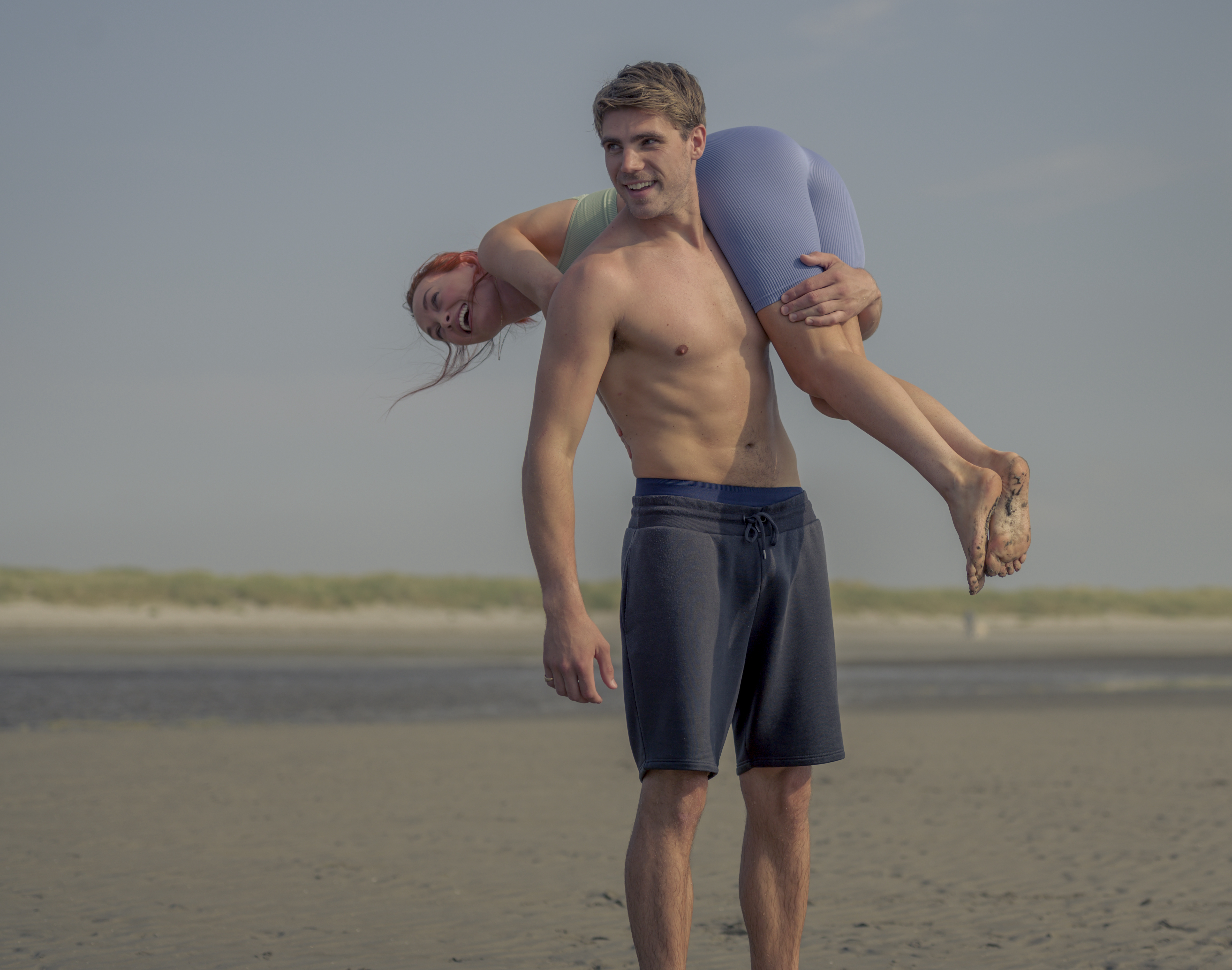 Seán (Jay Duffy) carries Áine (Elva Trill) on his shoulders at the beach.